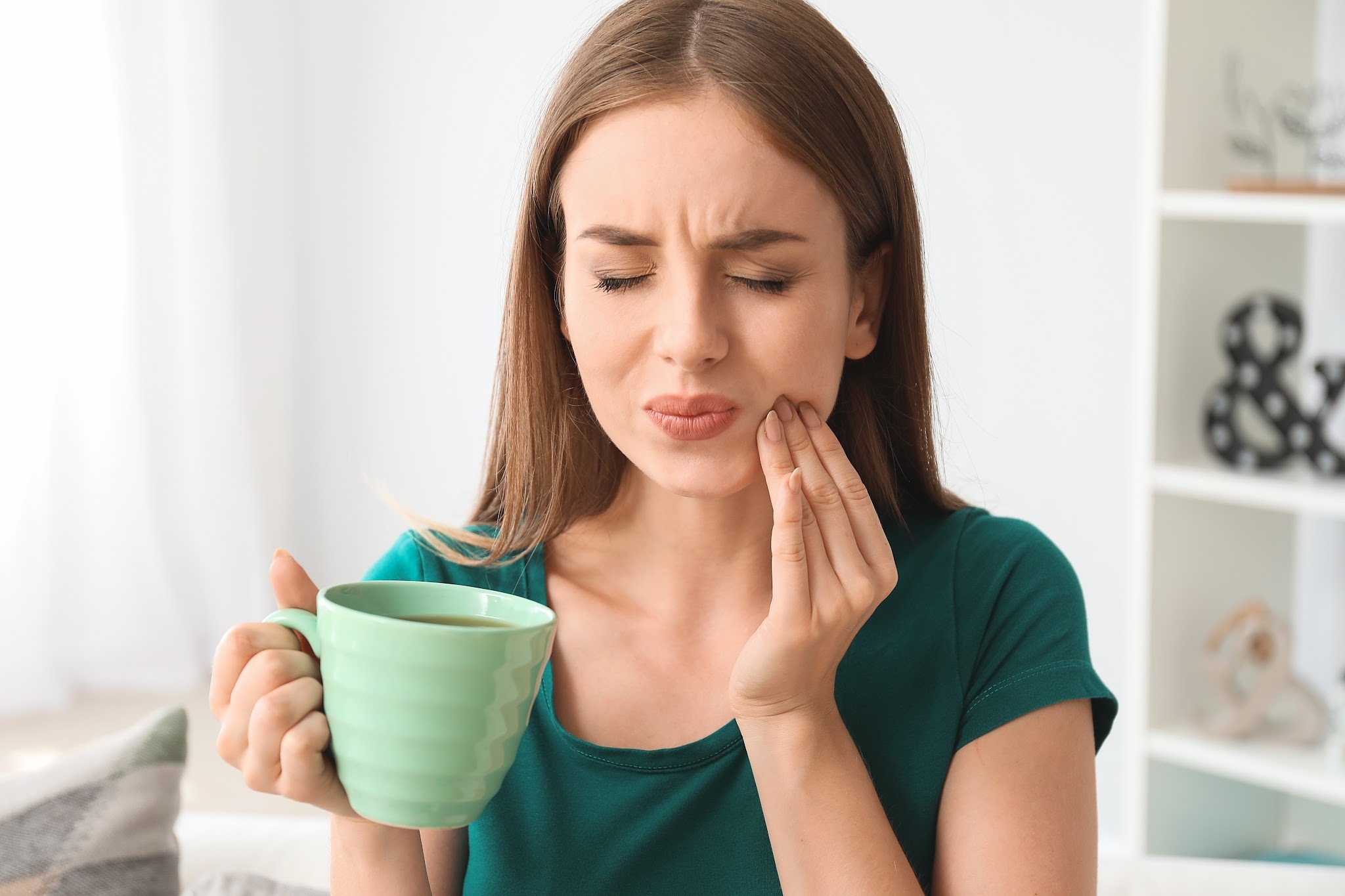Woman holding her jaw in pain while drinking, showing symptoms of toothache before visiting an emergency dentist in Purley