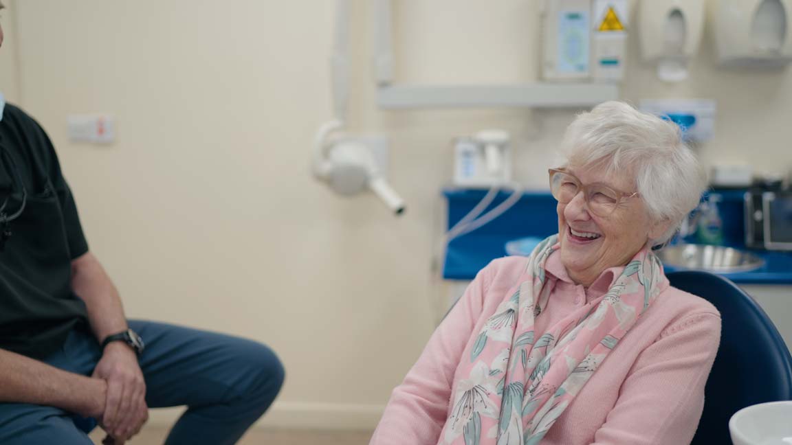 A happy retired female patient sitting in a dentist chair.