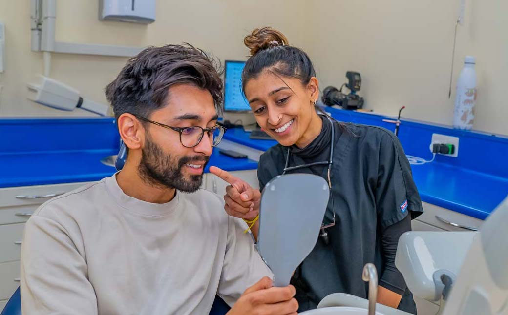 Dentist showing a happy male patient his smile in the mirror during a dental check-up following teeth whitening, at a Purley dental practice.