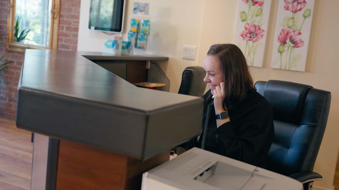 A smiling receptionist answers the phone in a welcoming dentist surgery.