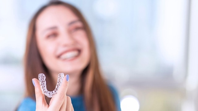 Smiling woman holding a clear Invisalign aligner for teeth straightening at a Purley dental clinic